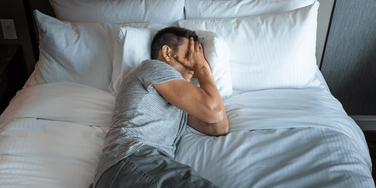 Person lying on bed, covering face.