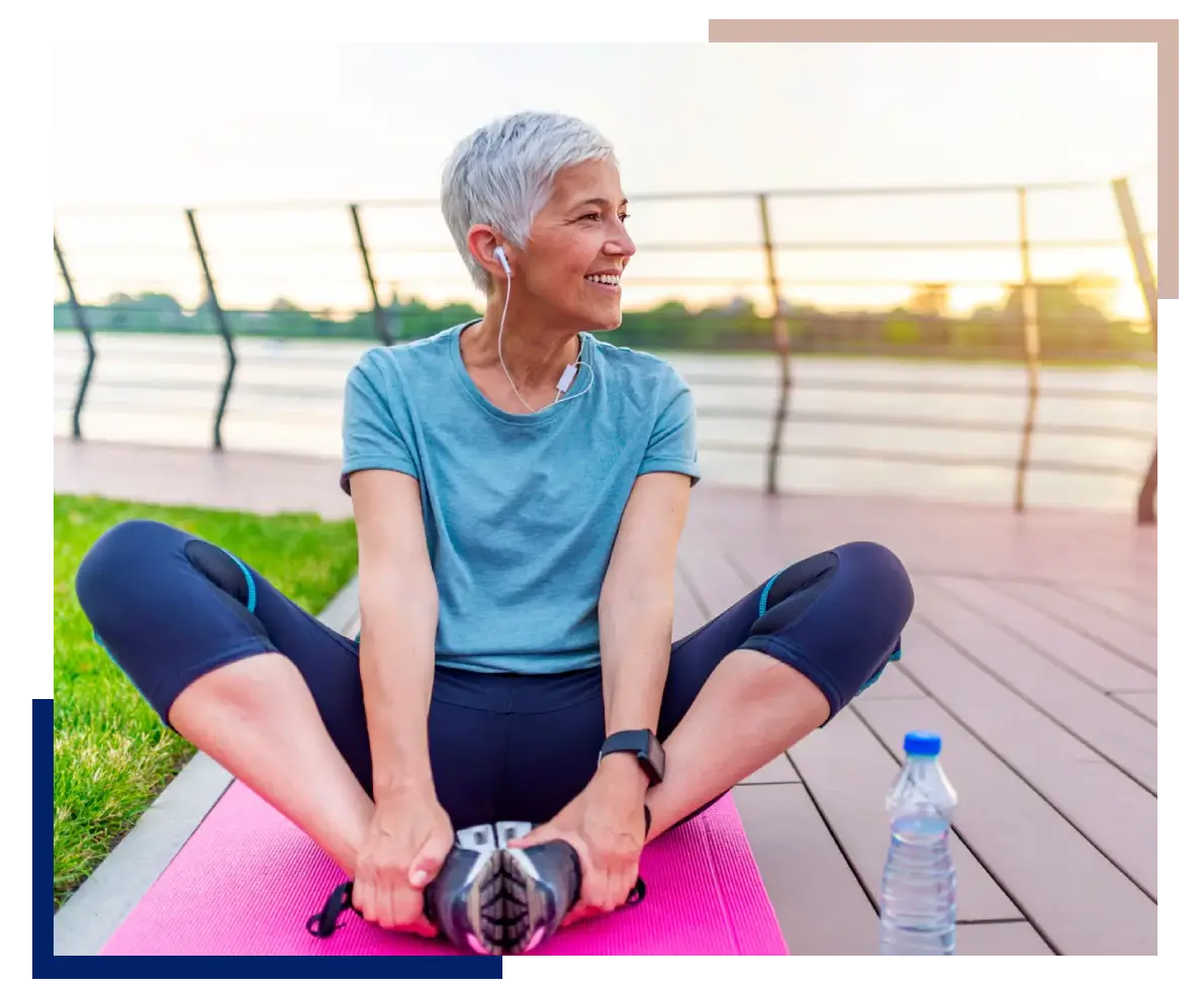 Older woman stretching on a yoga mat outdoors at sunset.